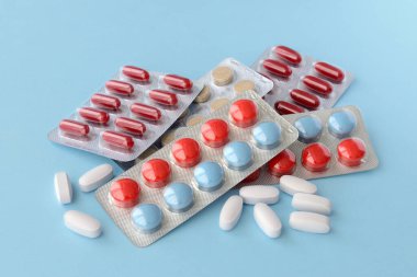 Çeşitli ilaç hapları, haplar ve kapsüller mavi arka planda.