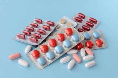 Çeşitli ilaç hapları, haplar ve kapsüller mavi arka planda.