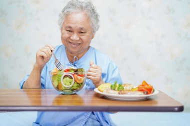 Asya kıdemli veya yaşlı yaşlı kadın kadın hasta umut ile kahvaltı sağlıklı yemek yeme ve mutlu otururken ve hastanede yatağa aç