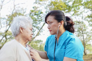 Doktor, parkta yürürken hastayı kontrol etmek için steteskop kullanıyor. Sağlıklı güçlü tıbbi konsept.