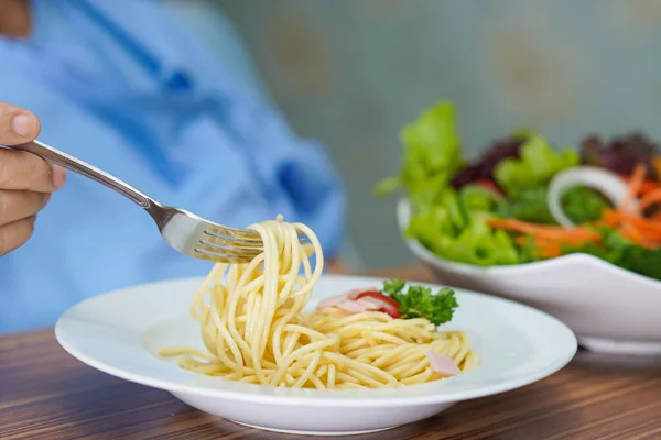Asian senior or elderly old lady woman patient eating carbonara spaghetti and salad vegetable breakfast healthy food with hope and happy while sitting and hungry on bed in hospital