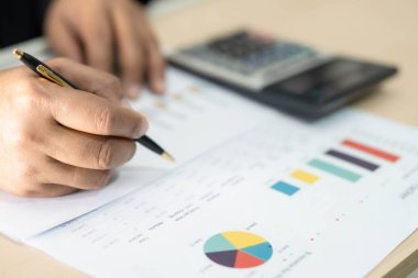 Asian accountant working and analyzing financial reports project accounting with chart graph and calculator in modern office : finance and business concept.