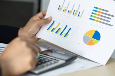 Asian accountant working and analyzing financial reports project accounting with chart graph and calculator in modern office : finance and business concept.