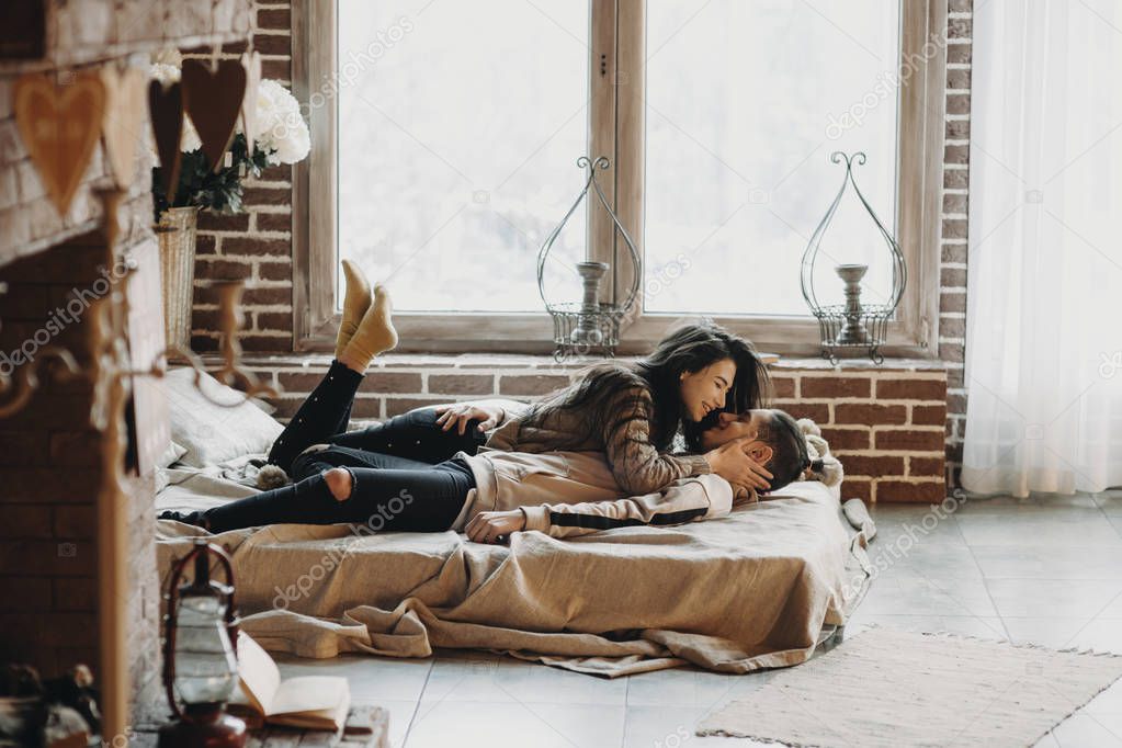 Couple laying in bed in a cozy room with big window.