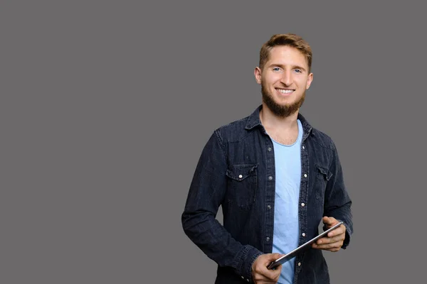 Um homem sorridente barbudo com olhos azuis segurando seu novo tablet e sendo aplaudido ao promover um item no espaço em branco cinza — Fotografia de Stock