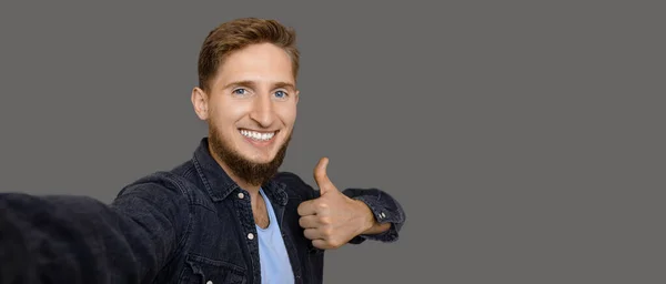 Een bebaarde blanke man met blauwe ogen die een selfie maakt en een gebaar maakt terwijl hij glimlacht op een grijze achtergrond met vrije ruimte — Stockfoto