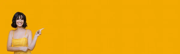 Härlig kaukasiska kvinna bär en klänning pekar på något med pekfingret och ler glatt på en gul tomt utrymme — Stockfoto