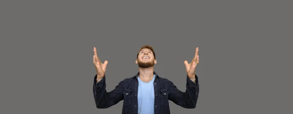 Hombre caucásico emocional con buena barba feliz por encontrar un nuevo trabajo, apuntando hacia un espacio en blanco sobre un fondo gris — Foto de Stock