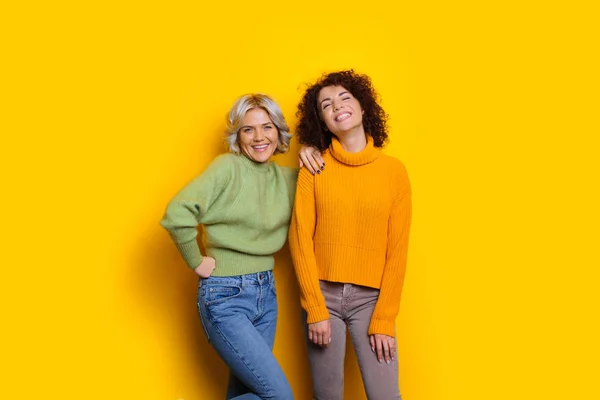 Schöne kaukasische Mädchen mit lockigen schwarzen Haaren posiert mit ihrem blonden Freund auf gelbem Hintergrund — Stockfoto