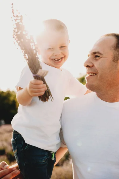 Krásný pohled na smějícího se syna, kterého drží jeho otec a který je objat sluncem a vůní levandule — Stock fotografie