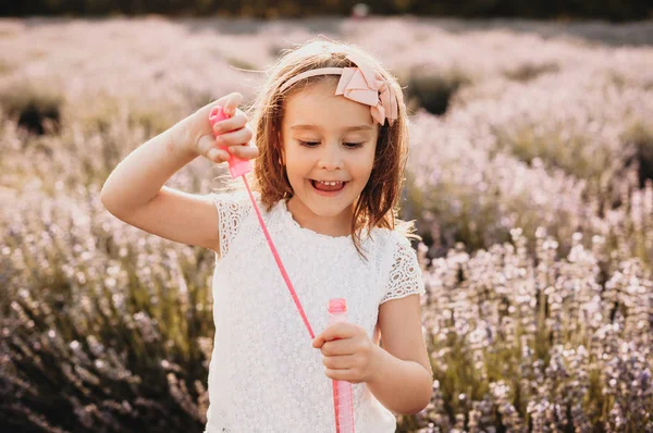 Uma jovem princesa alegre fazendo sopradores de bolhas em um fundo de lavanda polvilhado com sol — Fotografia de Stock