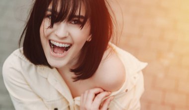 Hoş, esmer, beyaz bir kızın üst görünüşü. Güzel bir gülümsemesi var. Bir şeye hayran kalıyor.