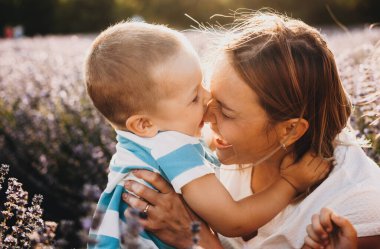 Nazik beyaz anne, arka plandaki lavanta tarlasında sarışın oğluyla gün ışığında oynuyor.