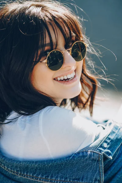 Närbild porträtt av en charmig kaukasisk kvinna klädd i solglasögon och leende glatt klädd i en blå jacka och vit t-shirt — Stockfoto