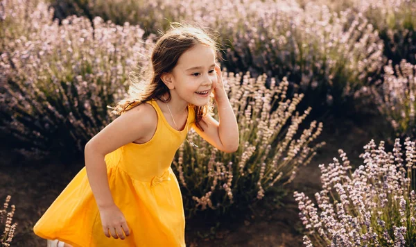 Linda menina caucasiana vestindo um vestido amarelo está jogando alegremente com seu cabelo em um campo de lavanda — Fotografia de Stock
