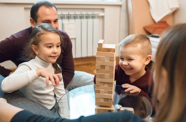 Leende kaukasier leker jenga med sin storasyster medan föräldrarna ser stolt ut. — Stockfoto