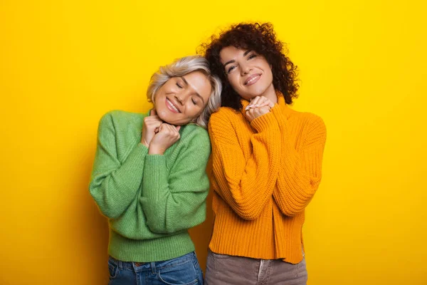 Nettes brünettes kaukasisches Mädchen mit lockigem Haar posiert in der Nähe ihrer besten Freundin und gestikuliert mit dem Zeichen enjoy, während sie auf gelbem Hintergrund posiert — Stockfoto