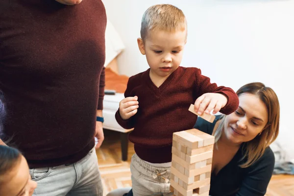 I genitori caucasici giocano a jenga con il loro figlio vestito con maglione rosso e jeans bianchi — Foto Stock