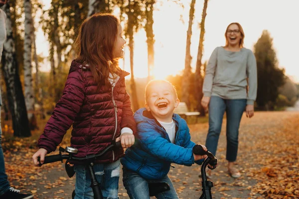 Allegra madre caucasica che insegna ai suoi bambini sorridenti ad andare in bicicletta durante una serata colorata autunnale. — Foto Stock