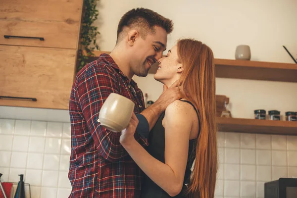 Sorridente coppia caucasica abbracciarsi e baciarsi in cucina mentre una colazione mattutina — Foto Stock