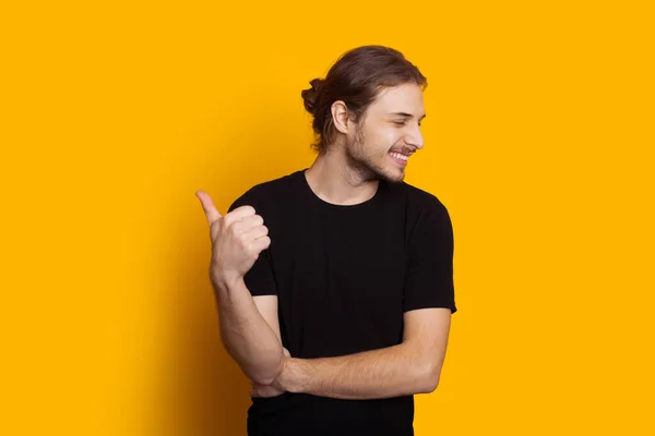 Vestido de homem branco preto com cabelos longos e barba está apontando para cima enquanto sorri e posando em um fundo amarelo — Fotografia de Stock