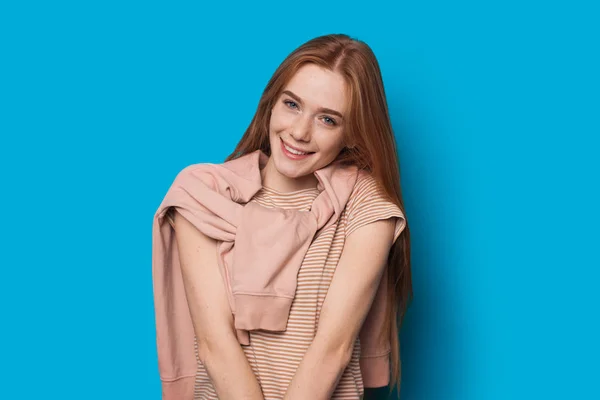 Encantadora chica caucásica con el pelo rojo y hermosa sonrisa está posando inocentemente sobre un fondo azul — Foto de Stock