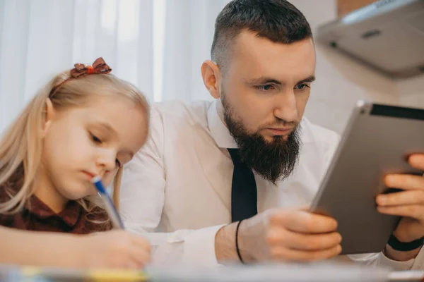 Homem caucasiano barbudo olhando para seu tablet de pé perto de sua filha enquanto ela está desenhando algo — Fotografia de Stock