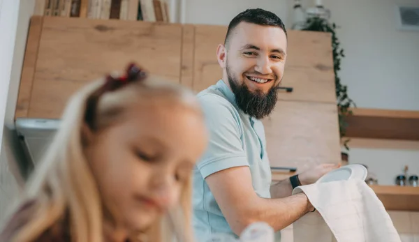 Barbudo hombre caucásico mirando y sonriendo a su pequeña hija mientras ella está dibujando algo —  Fotos de Stock