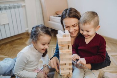 Kafkasyalı anne çocuklarına Jenga oynamayı öğretirken dikkatle dinliyorlar.