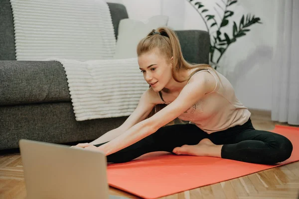 Ragazza caucasica allegra fare yoga sul pavimento mentre guardando il computer per alcuni esercizi — Foto Stock