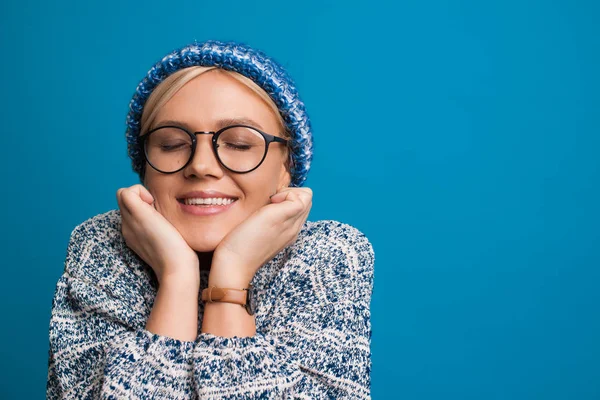 Preciosa mujer caucásica vestida con un suéter y sombrero azul está soñando con algo mientras posa sobre un fondo azul — Foto de Stock