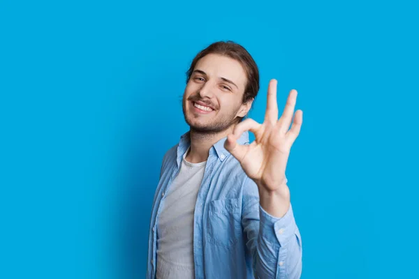 Hermoso chico caucásico gesto signo de aprobación mientras sonríe y posando sobre un fondo azul — Foto de Stock