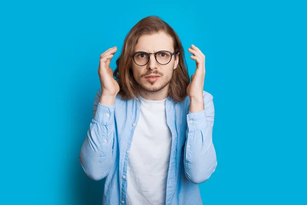 Bonito homem caucasiano com barba e cabelos longos é chocado por algo enquanto posando em um fundo azul — Fotografia de Stock
