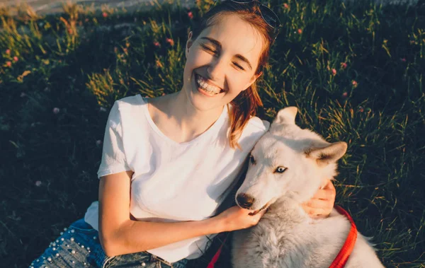 Souriant fille caucasienne vêtue d'un t-shirt blanc joue avec son chien tout en étant allongé sur l'herbe dans le parc — Photo