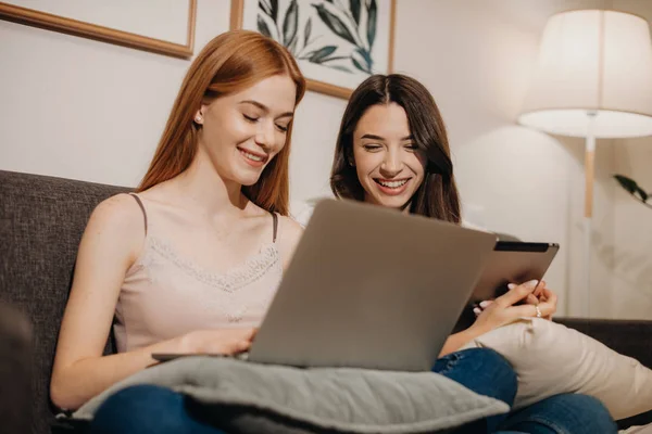 Rudowłosy biały dziewczyna za pomocą laptopa w pobliżu jej piękny brunetka przyjaciel z tabletem — Zdjęcie stockowe