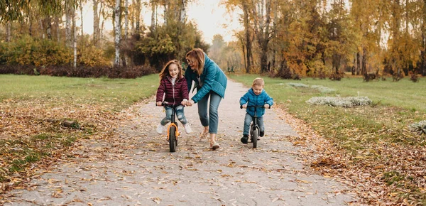 Kafkasyalı anne, parkta yürürken çocuklarına bisiklet sürmeyi öğretiyor. — Stok fotoğraf