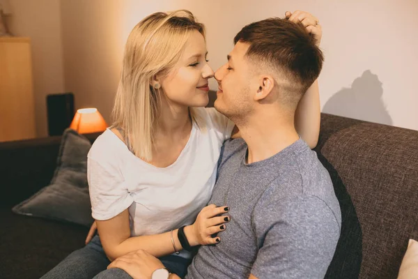 Casal caucasiano deslumbrante sentados juntos em um sofá e beijando uns aos outros durante uma noite quente juntos — Fotografia de Stock