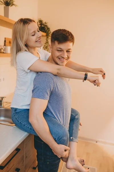 Bájos szőke lány ölelgeti a szeretőjét, miközben a konyhában ül, és együtt töltik az időt. — Stock Fotó