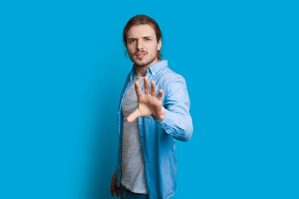 Homem caucasiano olhando para a câmera e gesticulando como se quisesse parar algo enquanto posava em uma parede azul — Fotografia de Stock