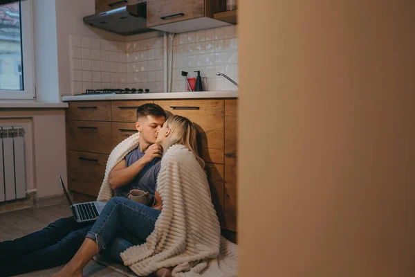 Stilig kaukasiskt par täckt med ett täcke kysser varandra i köket på golvet — Stockfoto