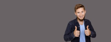 Kahverengi sakallı ve mavi gözlü beyaz adam, gri duvarda boş bir alanda poz verirken aynı işareti alıyor.