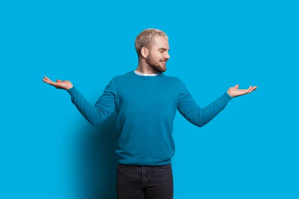 Homem caucasiano com cabelo loiro e barba está gesticulando um equilíbrio com as mãos olhando e sorrindo alegremente em uma parede azul — Fotografia de Stock