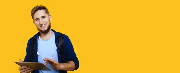 Homem caucasiano com barba agradável e olhos azuis está segurando um tablet enquanto posando perto do espaço livre amarelo — Fotografia de Stock