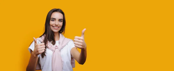 Ragazza caucasica con bel sorriso sta gesticolando con mano il segno simile mentre posa su una parete gialla con spazio libero — Foto Stock