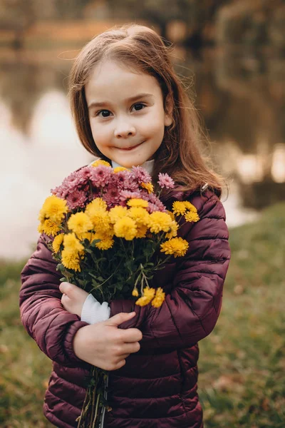 Menina caucasiana alegre olhando para a câmera enquanto posando na frente de um lago com um monte de flores — Fotografia de Stock