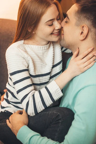 Encantadora dama de jengibre con pecas está sentada en un sofá con su marido y besándolo mientras se abrazan —  Fotos de Stock