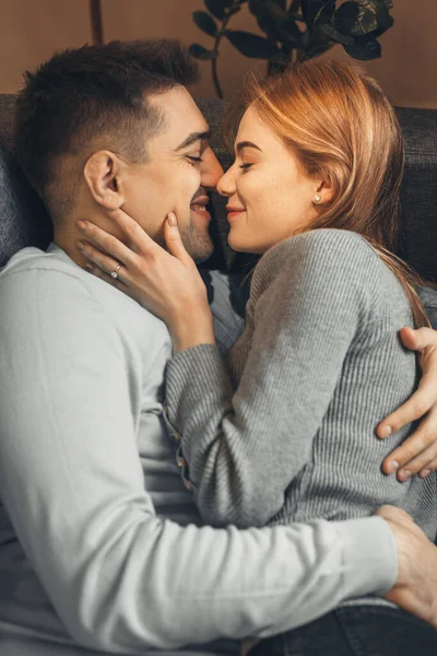 Hermoso chico caucásico sosteniendo a su novia con el pelo rojo y pecas mientras está acostado en el sofá —  Fotos de Stock