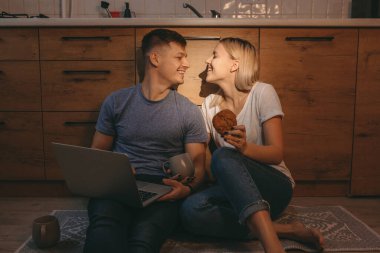 Sarışın, beyaz bir kız elinde pasta, mutfakta yerde otururken sevgilisine gülümsüyor.