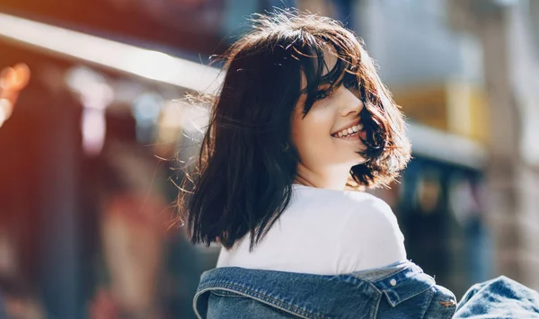 Cute caucasian girl poasing back to camera while smiling in a blue jeans jacket in the city — Stockfoto