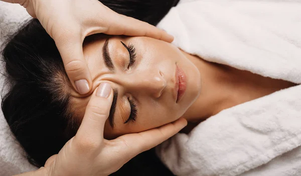 Kavkazská dívka s černými vlasy, která spí během masáže obličeje v lázních — Stock fotografie